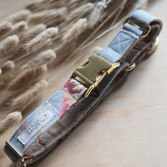 large old floral print in multicolor pinks, burgundy, beige, and muted green, on a dusty blue background. Colors are muted in appearance, outer fabric is cotton canvas. shown with shiny gold, heavy duty metal hardware. this is a Martingale, or Cinch dog collar