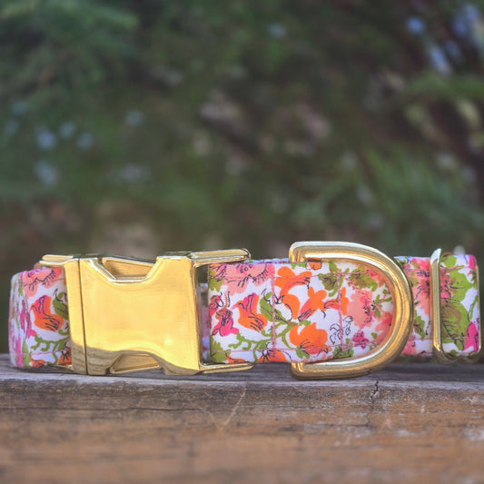 vintage floral-patterned dog collar in shades of pink, orange and coral, with bright spring green leaves, with a gold buckle on a wooden surface with a blurred natural background