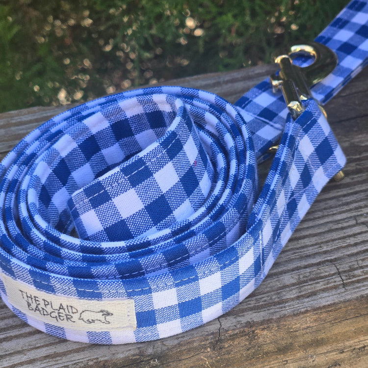 Royal blue and white gingham checkered dog leash on a wooden surface with a blurred natural background
