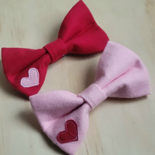 valentines day themed dog bow ties made with soft cotton flannel in solid pattern. shown in red with small pink heart appliqued to the bottom corner, or bubblegum pink with a red heart on the bottom corner