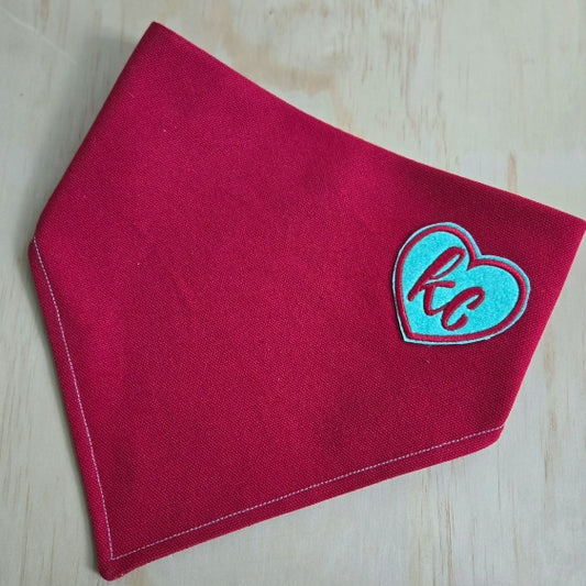 durable red cotton canvas over the collar dog bandana with adorable embroidered iron on patch on upper right corner. patch is a heart with cursive  KC in matching red, and background is sparkly light teal. KC Current themed bandana. 