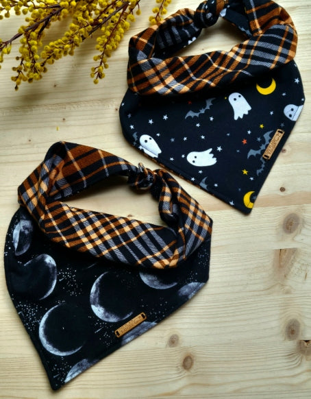 reversible dog bandanas in two options, spooky ghosts and moon phases. Moon phases feature the moon in different celestial phases and spooky ghosts features cute cartoon ghosts, bats and moons. both bandanas reverse to orange and black complimentary cotton flannel