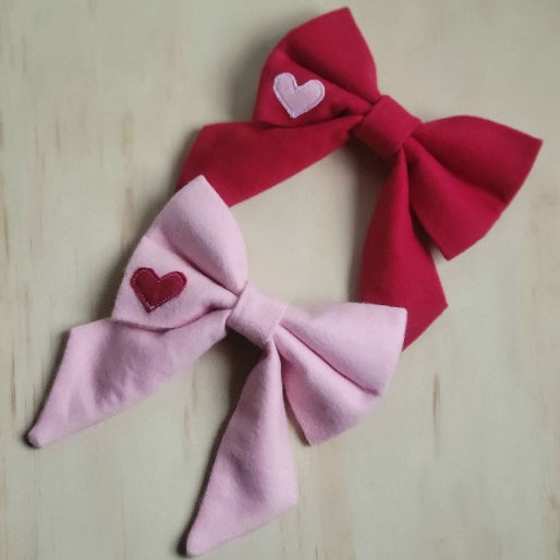 solid cotton flannel fancy girl dog bows. perfect for valentines day, shown in solid red with contrasting bubblegum pink heart appliqued, and bubblegum pink with small red heart appliqued. sailor bow