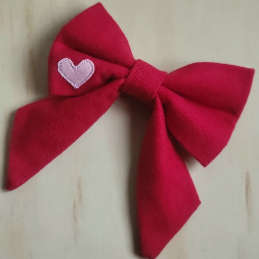 solid red cotton flannel fancy girl dog bow. small contrasting bubblegum pink heart appliqued on bottom left corner of bow 