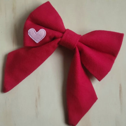 solid red cotton flannel fancy girl dog bow. small contrasting bubblegum pink heart appliqued on bottom left corner of bow 